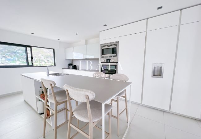 View of the open-plan kitchen equipped with high chairs, a central island with sink and full appliances in a luxury villa in the West Indies.