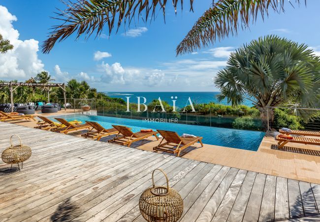 View of the wooden terrace with wooden deckchairs, overlooking the pool and the ocean, in a top-of-the-range villa in the West Indies