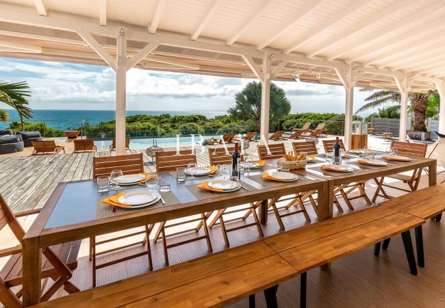 Vista de la mesa de comedor exterior para 12 personas con una magnífica vista de la piscina y el océano en una villa de lujo en las Antillas