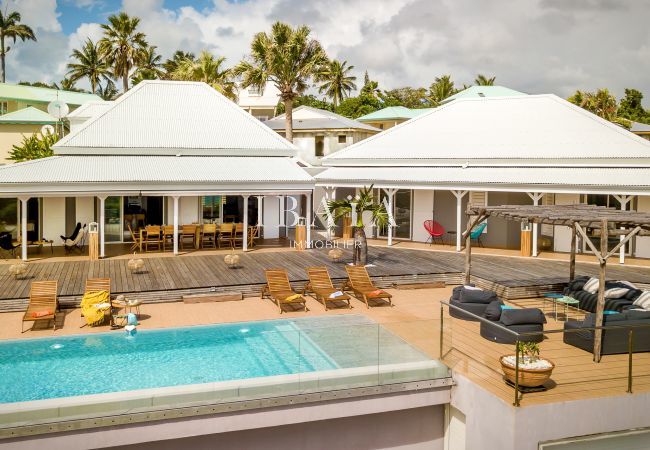 View of the front of the villa with swimming pool, outdoor living area under a wooden pergola in a luxury villa in the West Indies.