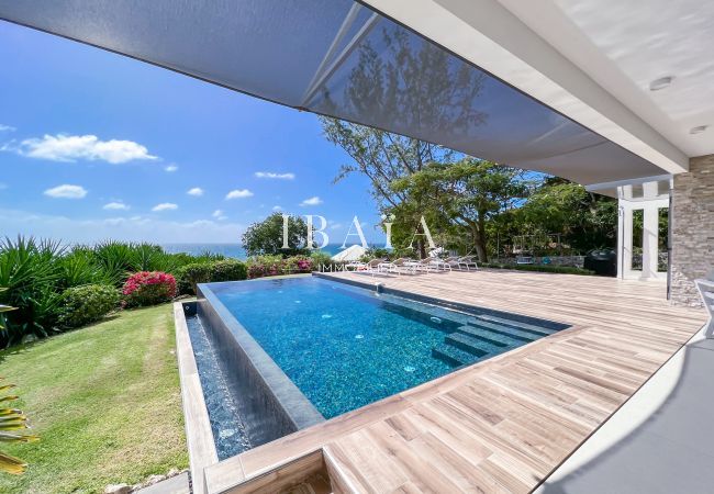 View from wooden terrace of infinity pool with well-kept tropical garden and ocean