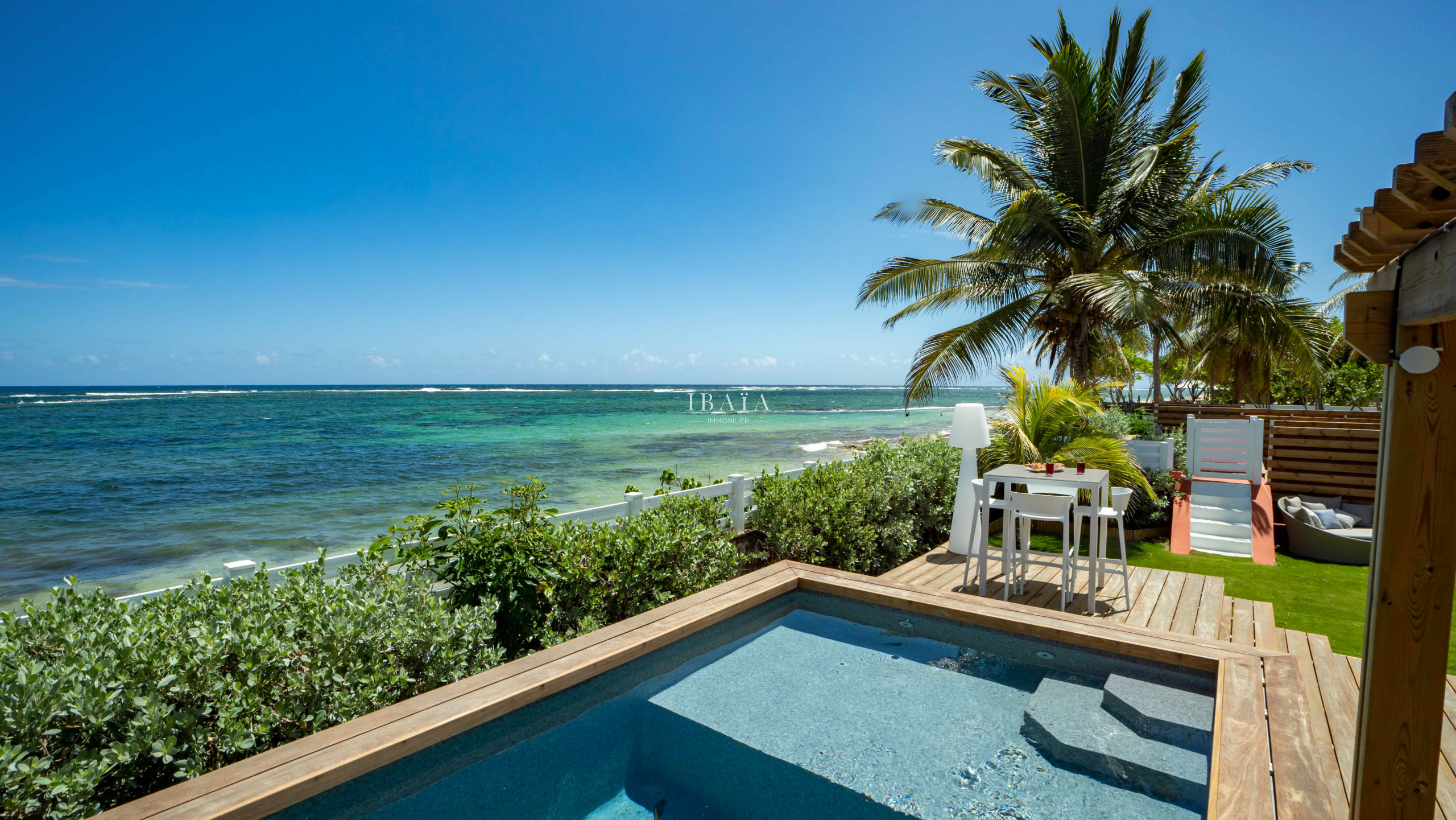 View of the pool and sea from the poolside terrace, with a 4-seater high table in our top-of-the-range villa in the West Indies.