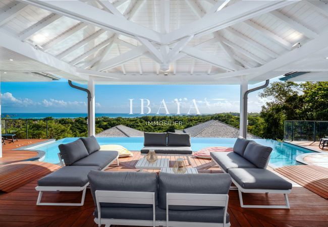 Covered terrace with modern furniture overlooking a pool and panoramic view.