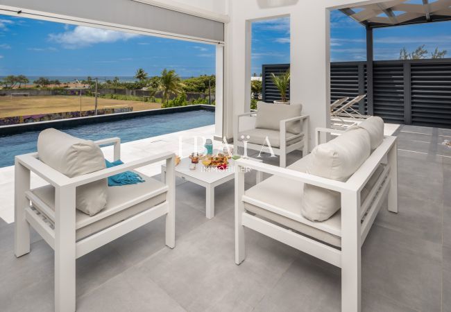 Outdoor relaxation area with white furniture near a pool, sea view in the background.