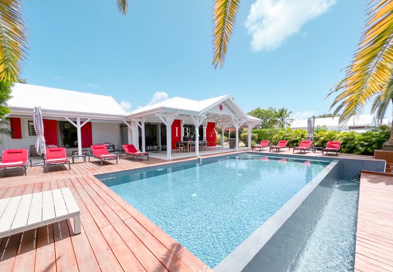 View of the infinity pool surrounded by red deckchairs and the elegant facade of the upscale villa in the West Indies.