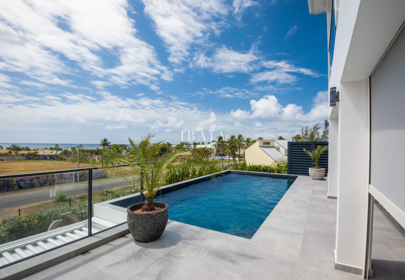 View of a terrace with pool overlooking the beach and cloudy blue sky.