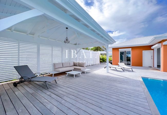 Terraza de madera con tumbonas y salón exterior junto a la piscina en una villa de alta gama en las Antillas, para disfrutar del máximo relax