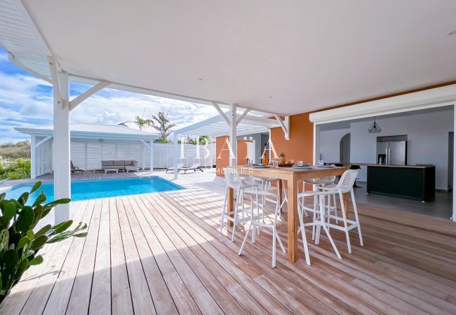Vista de la piscina con mesa y sillas altas en la terraza de madera de una villa de lujo en las Antillas