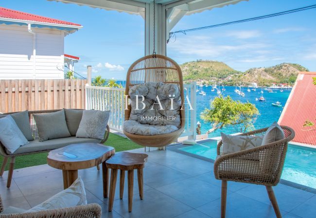 Vista de la terraza con salón exterior, silla colgante, piscina y vistas a la bahía en una villa de lujo en las Antillas