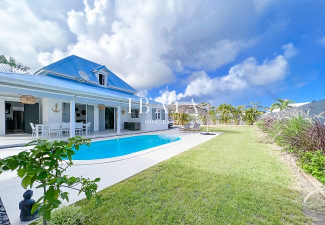 Vista de la piscina frente a esta villa de alta gama en las Antillas, con una mesa de comedor para relajarse y comer al aire libre.
