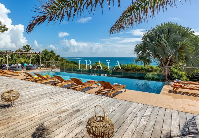 Vista de la terraza de madera con tumbonas de madera, con vistas a la piscina y al océano, en una villa de alta gama en las Antillas.