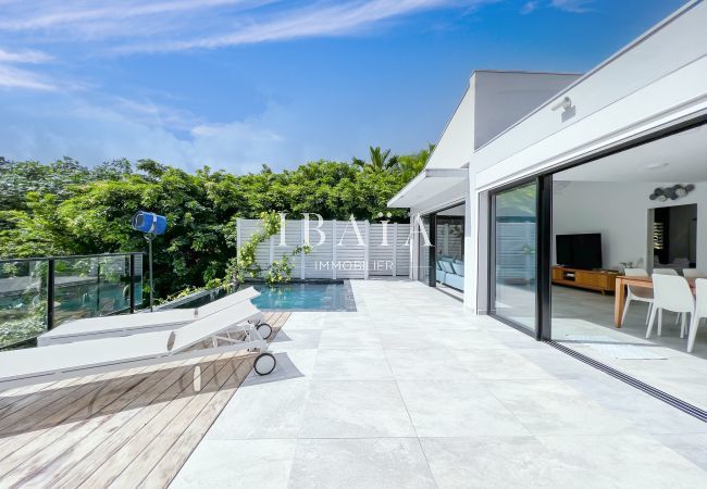 Vista sobre la terraza exterior, la piscina y sus 2 tumbonas y vista sobre el comedor y el salón abiertos al exterior gracias a grandes aberturas