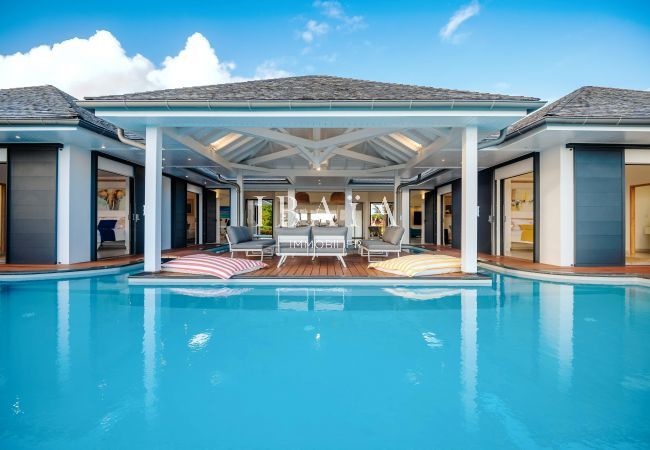 Casa de lujo con piscina turquesa, terraza de madera e interiores visibles.