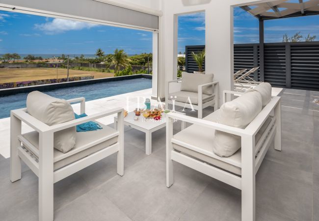 Área de descanso al aire libre con muebles blancos cerca de una piscina, vista al mar en el fondo.