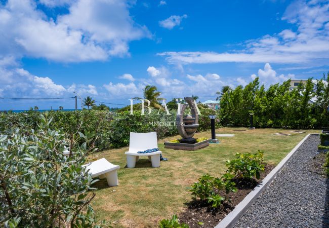Jardín tropical con una escultura moderna, una silla blanca y vistas al océano.