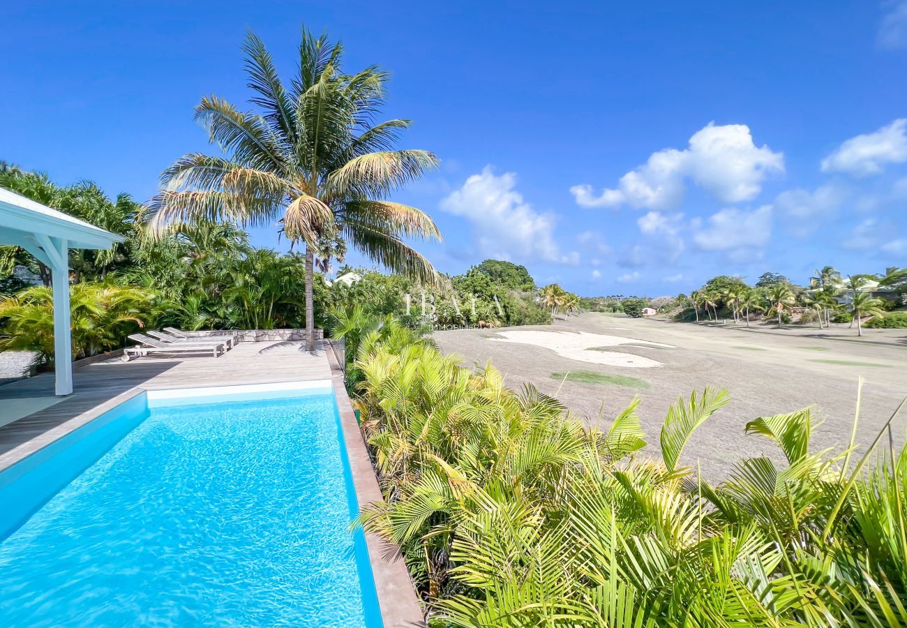 Vista del campo de golf internacional de Saint-François, la piscina y las tumbonas de la terraza de madera de una villa de lujo en las Antillas.