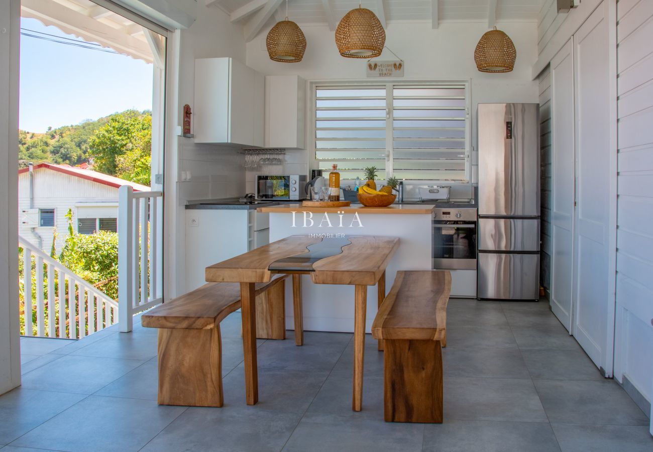 Vista de la zona de comedor y cocina con mesa y banco de madera en una villa de alta gama en las Antillas, para una experiencia culinaria refinada.