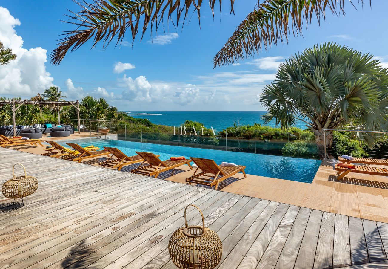 Vista de la terraza de madera con tumbonas de madera, con vistas a la piscina y al océano, en una villa de alta gama en las Antillas.