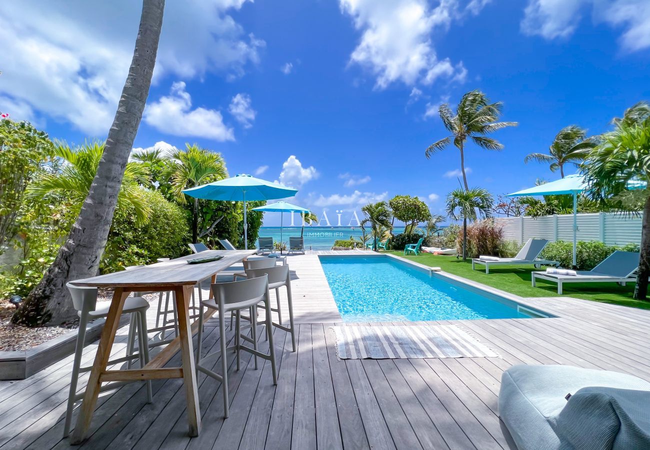 Sillas y mesas altas en una terraza de madera junto a la piscina con vistas al mar, a la sombra de cocoteros - Villa de lujo en las Antillas francesas