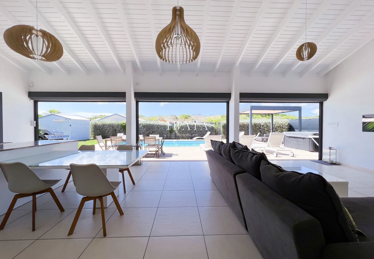 Vista panorámica del salón interior y la mesa de comedor, con vistas a la terraza y la piscina, en una villa de alta gama en las Antillas.