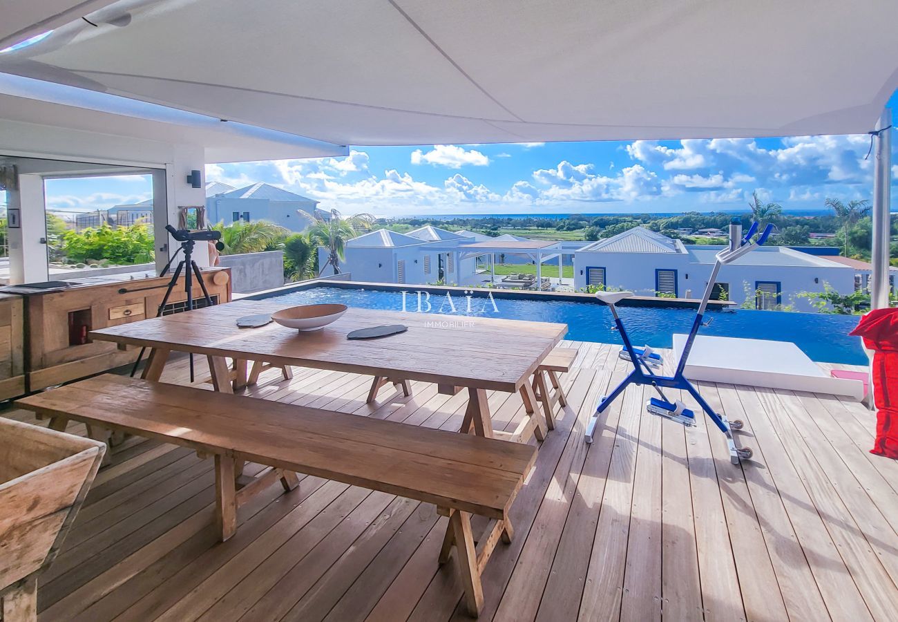 Terraza cubierta con mesa de madera y piscina infinita con vistas al paisaje costero