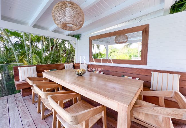 Grande table en bois pour 8 personnes avec chaises en bois et grands bancs face à la piscine, miroir encadré en bois et lustre en osier dans une villa