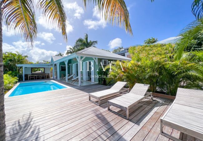 Vue de la terrasse en bois, de la maison, des transats en bois et de la salle à manger en bois dans un jardin tropical, dans une villa haut de gamme a