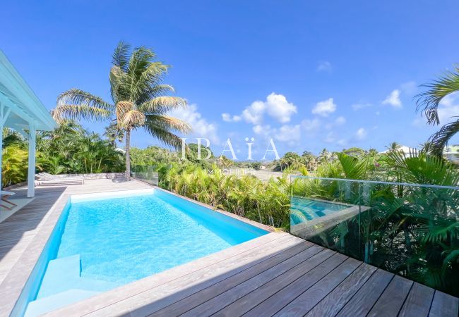 Vue sur la piscine et le golf de Saint-François depuis la villa de luxe, entourée d'une terrasse en bois et de cocotiers dans les Antilles