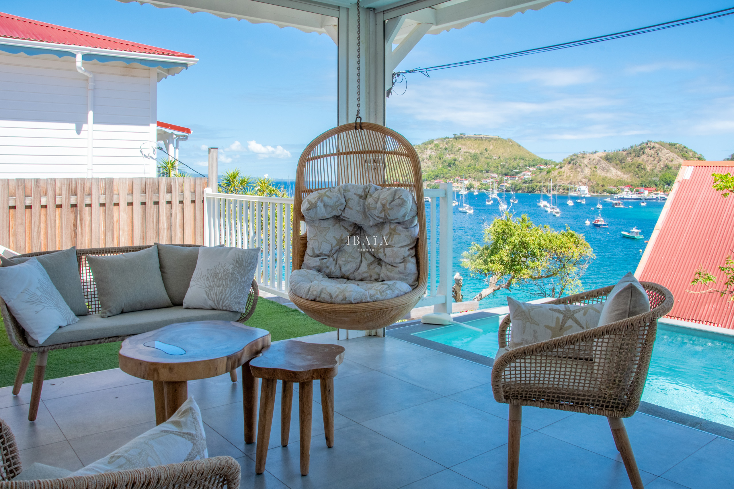 Vue de la terrasse avec salon d'extérieur, fauteuil suspendu, piscine et vue sur la baie dans une villa haut de gamme aux Antilles