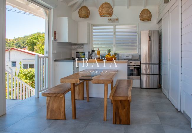 Vue du coin repas et de la cuisine avec table et banc en bois dans une villa haut de gamme aux Antilles, pour une expérience culinaire raffinée