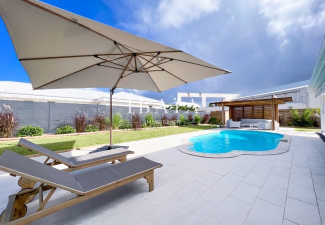 Vue sur la piscine, un transat, un parasol et un salon de jardin ombragé dans une villa haut de gamme aux Antilles, pour des moments de détente en ple