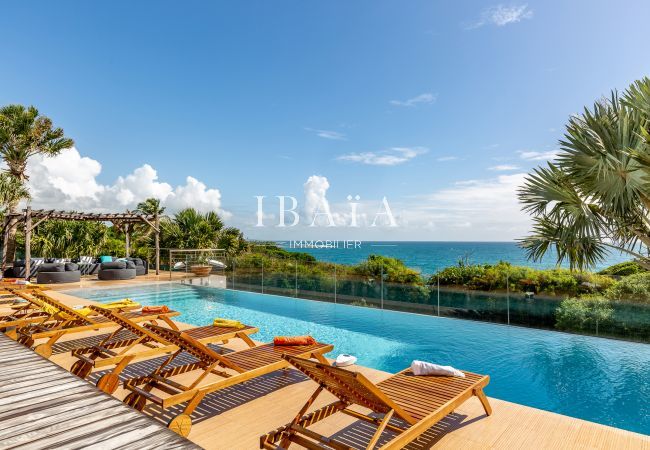 Vue sur une piscine à débordement, l'océan et 8 transats en bois dans une villa de luxe aux Antilles, pour des moments de détente au bord de la piscin