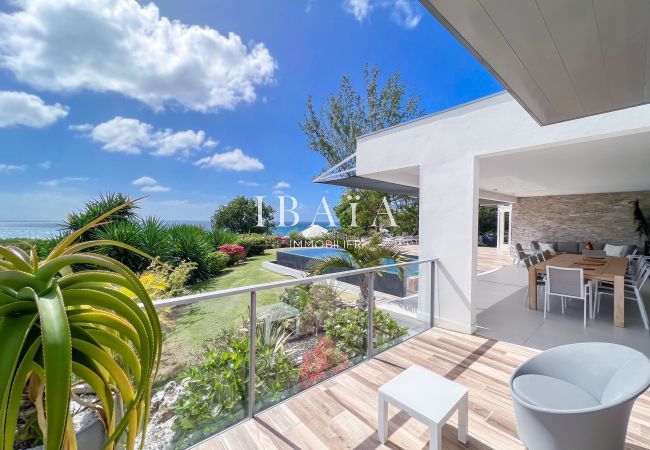 Vue depuis terrasse ombragée sur piscine et mer dans jardin tropical entretenu