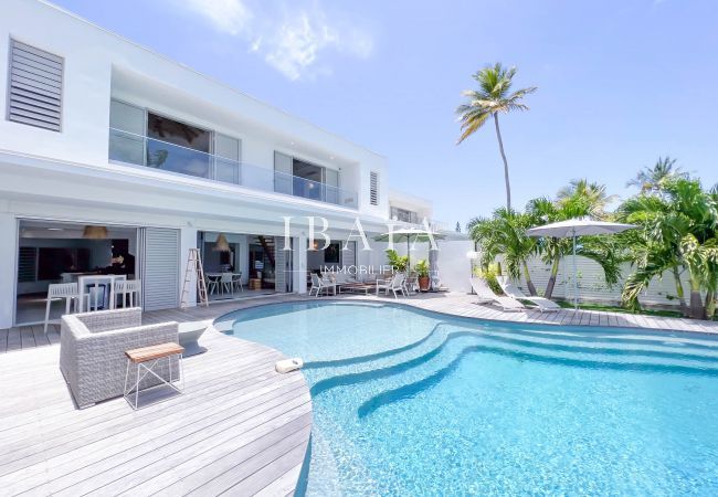 Vue extérieure de la villa avec terrasse en deck, salon, transat et parasol près de la piscine