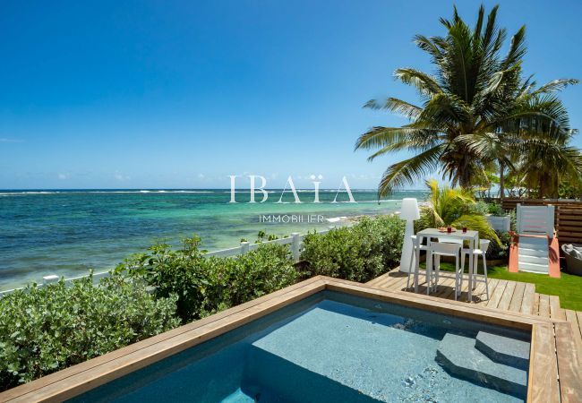 Vue de la piscine et de la mer depuis la terrasse en bord de piscine, avec une table haute 4 places de notre villa haut de gamme aux Antilles.