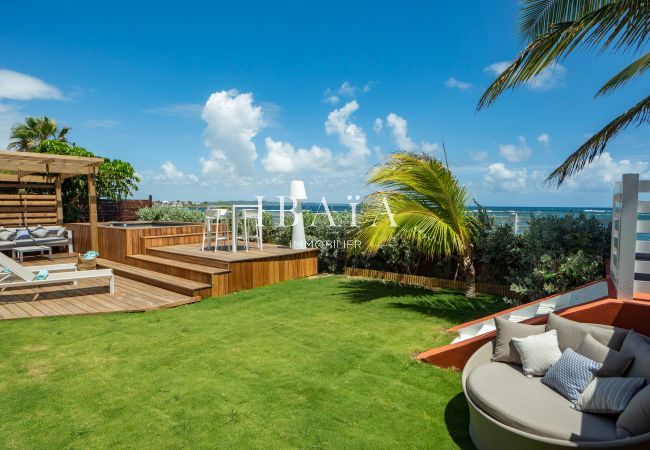 Vue du jardin avec 2 transats sur la terrasse en bois et un grand lit extérieur de notre villa de luxe en bord de mer aux Antilles.