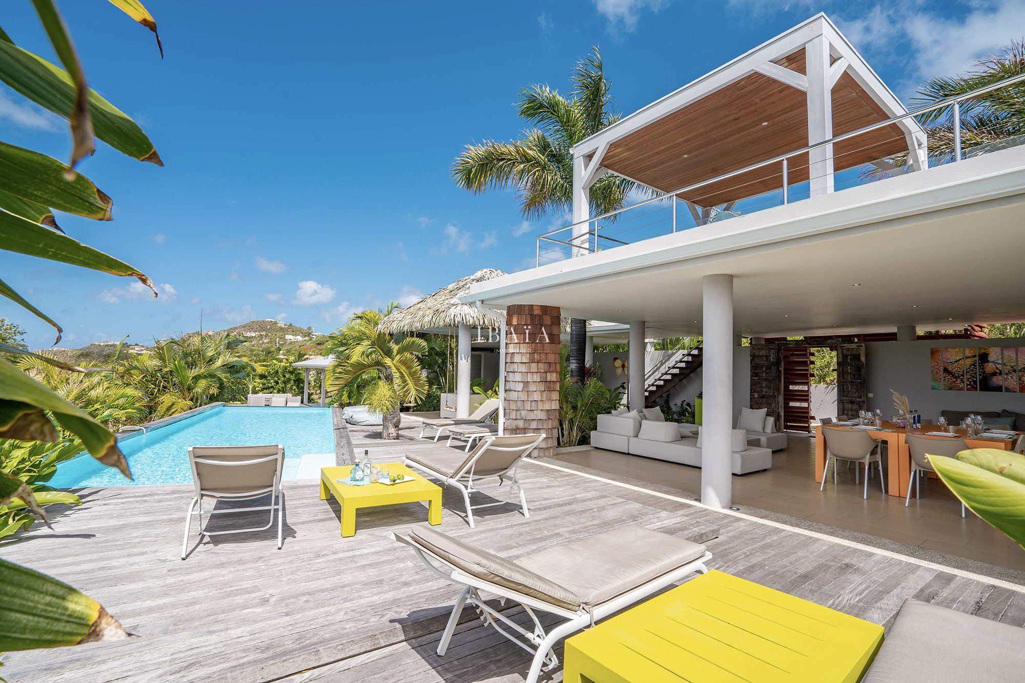 Vue de la terrasse en bois avec 4 transats, tables à café, piscine et terrasse ombragée avec salon d'extérieur et table à manger