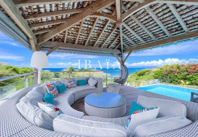 Vue d'un salon de jardin en rond de 8 places au bord de la piscine sous un patio en bois, offrant une vue sur la mer dans notre villa haut de gamme au