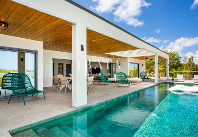 Vue de la superbe piscine à débordement rectangulaire avec céramique, entourée d'une grande terrasse avec fauteuils et salle à manger dans notre villa