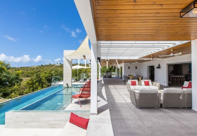 Piscine à débordement avec terrasse en bois et salon extérieur sous un patio - Villa haut de gamme aux Antilles