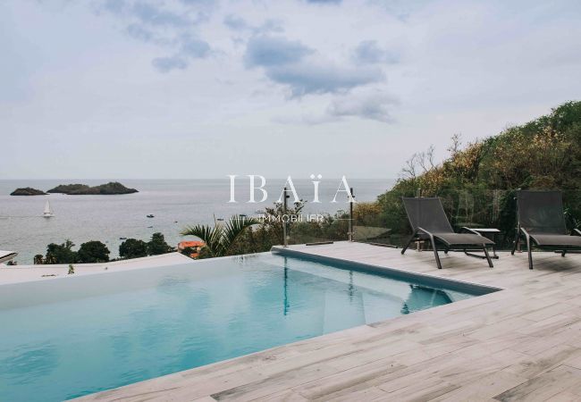 Vue panoramique depuis la terrasse en bois sur les îlets Pigeons et la piscine, dans une villa haut de gamme aux Antilles