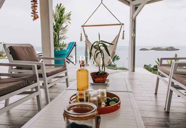 Salon d'extérieur avec fauteuils, table basse et hamacs offrant une vue sur les îlets Pigeons, dans une villa haut de gamme aux Antilles