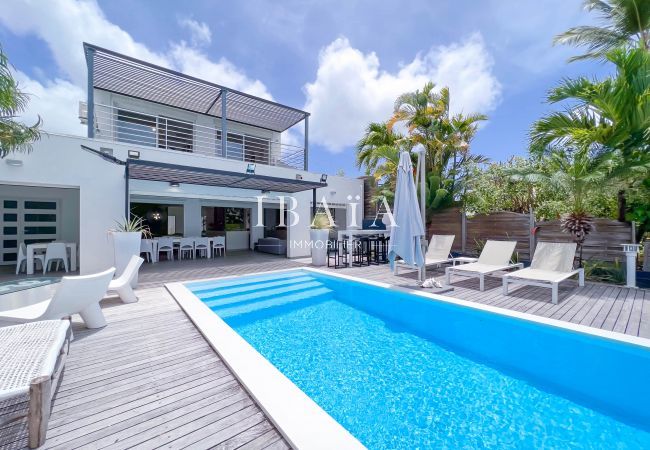 Piscine de la villa, terrasse en bois, maison à deux niveaux, transats, parasols et végétation tropicale