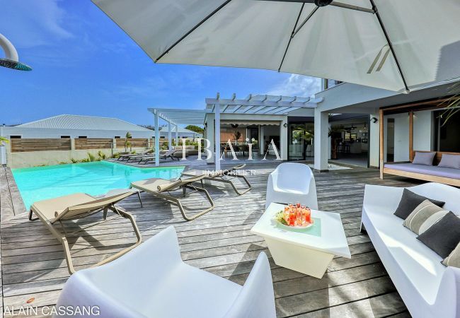 Vue sur une luxueuse maison avec piscine, coin salon extérieur et parasol ouvert