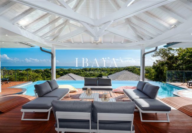 Terrasse couverte avec mobilier moderne donnant sur une piscine et une vue panoramique.