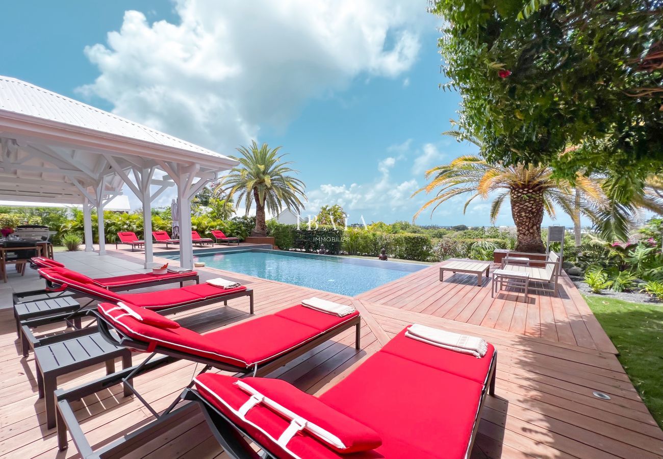 Vue sur la piscine, les transats rouges et le fauteuil de jardin autour de la piscine à débordement avec un jardin tropical dans une villa haut de gam