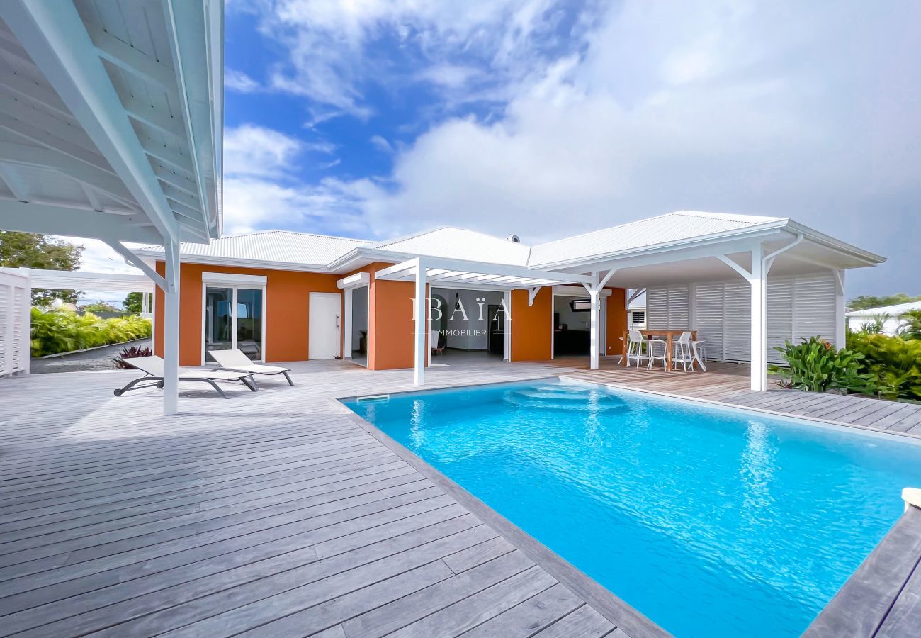Vue de la terrasse en bois avec piscine, transats, table haute et chaise haute dans une villa haut de gamme aux Antilles