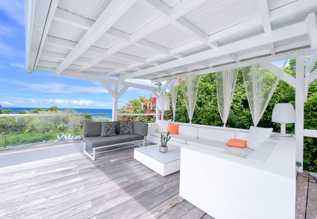 Vue du salon de jardin sous le patio sur une terrasse en bois avec vue sur la mer dans notre villa haut de gamme aux Antilles