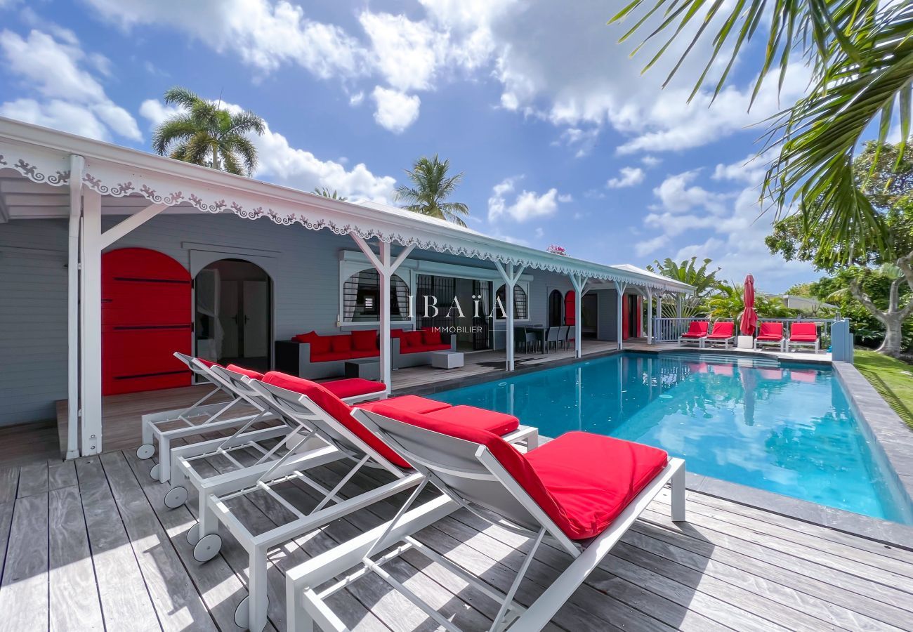 Transats rouges en bord de piscine sur terrasse en bois - Villa haut de gamme aux Antilles
