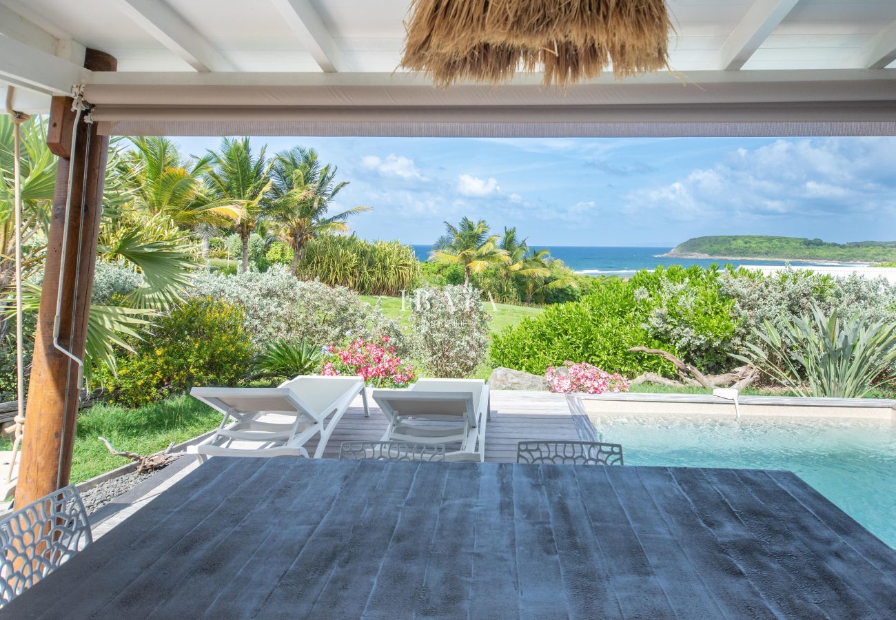 Terrasse couverte avec table, transats, piscine et vue mer dans un jardin tropical